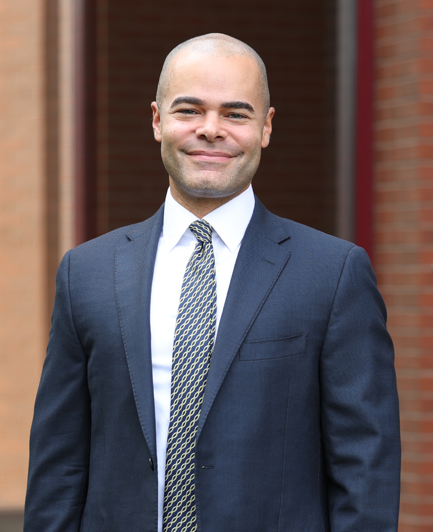 Adrian Ohmer stands in a sport coat and tie, smiling